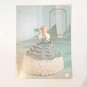 May include: A vintage calendar page featuring a doll in a crocheted dress. The doll has blonde hair and is wearing a blue and white dress. The calendar shows the month of September 1992.