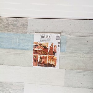 May include: A McCall's Home Decorating pattern booklet featuring images of home decor projects. The cover includes the text "Decorating Essentials" and "Les Essentiels de Decoration". The booklet has a white background with images of home decor.