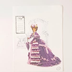 May include: A vintage calendar page featuring a doll in a purple and pink crocheted Victorian-style gown, holding a matching parasol. The calendar displays the month of May, with the year 1995 visible. The doll has a matching hat and cape.