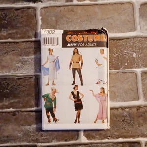 May include: A rectangular sewing pattern envelope for Jiffy Costumes for Adults, numbered 7382. The white packaging features illustrations of six different costume styles, including historical and themed outfits, with a barcode in the top left corner.