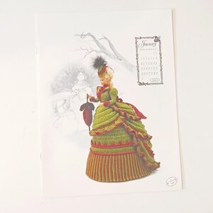 May include: A printed page featuring a crochet doll in a green and red dress, holding a red umbrella. The doll is set against a winter landscape with a calendar that reads "January 1891".