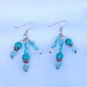 May include: A pair of dangle earrings with turquoise and light blue beads. The earrings have silver hooks and silver accents.