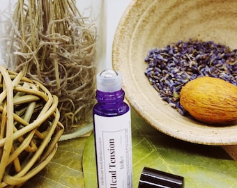 May include: A purple glass roller bottle with a white label that reads "Head Tension - Roller - Wellness and Holistic Care". The bottle is sitting on a green leaf.