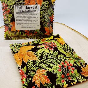 Pode incluir: Um sachê botânico Fall Harvest com fundo preto, com folhas laranja e amarelas, bagas vermelhas e folhagem verde. O sachê é feito de tecido de algodão e foi projetado para perfumar gavetas, armários ou atuar como um ambientador.