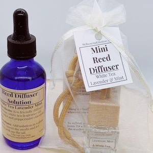 Könnte beinhalten: Ein Mini-Rieddiffusor mit einem Duft von weißem Tee, Lavendel und Minze. Der Diffusor kommt in einer kleinen, durchsichtigen Glasflasche mit einem braunen Holzdeckel und einer braunen Schnur. Die Flasche ist in einem weißen Organzasäckchen mit einem weißen Etikett verpackt, auf dem "Mini Rieddiffusor Weißer Tee Lavendel & Minze" steht.