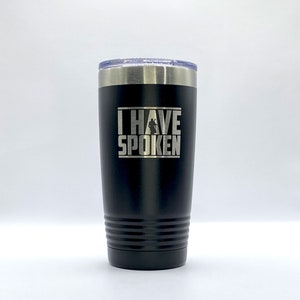May include: A black stainless steel tumbler with a silver lid. The tumbler has a white graphic that says "I HAVE SPOKEN" with a silhouette of a person in the middle of the text.