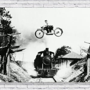 May include: A black and white photograph of a vintage steam locomotive train engine traveling on a track. A person is riding a motorcycle over a bridge in the background.