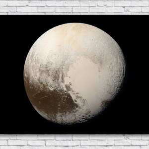 May include: A print of the dwarf planet Pluto against a black background. The planet's surface is a mix of light tan, brown, and white, with a large, lighter-colored region. The print is displayed on a white brick wall.