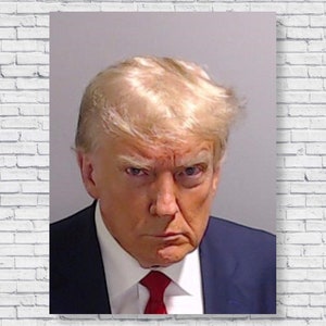 May include: A close-up portrait of a man with blond hair wearing a dark suit and a red tie. He has a serious expression on his face.