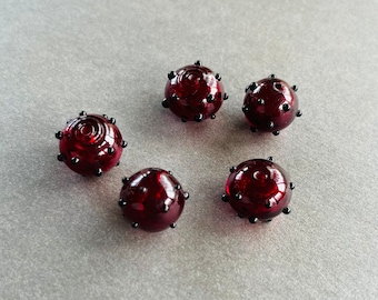May include: Five red glass beads with black dots. The beads are round and have a textured surface.