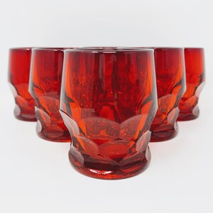 May include: Set of six red glass tumblers with a faceted design. The glasses are arranged in a row, with the front glass in focus.