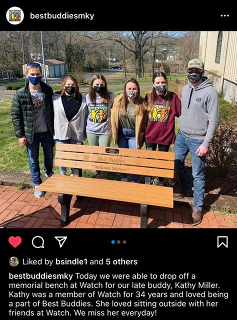 May include: A group of people stand in front of a wooden bench with the words "Best Buddies" and "Inclusion Matters" engraved on it. The bench is a memorial for a late friend.