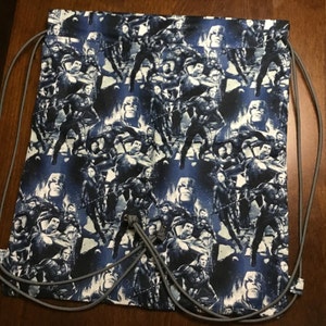 Puede incluir: Una bolsa azul con cordón con un patrón repetido de Capitán América y otros personajes. La bolsa tiene un cierre de cordón gris y está hecha de tela. El fondo es de color azul oscuro.