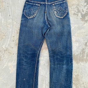 May include: A pair of blue denim jeans with a brown leather patch that says "Lee" on the back. The jeans have a faded and distressed look.