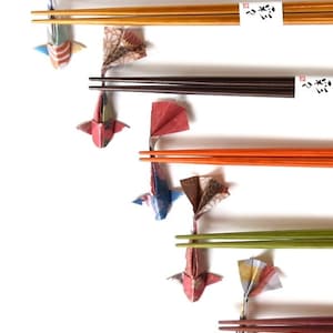 May include: A collection of colorful origami koi fish attached to sets of chopsticks. The chopsticks are in various colors, including brown, orange, and green. The origami fish are made from patterned paper in shades of red, blue, and brown.
