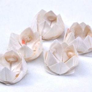May include: Five white paper lotus flower shapes, each with a small, round, white center. The flowers are arranged in a semi-circle on a white surface.