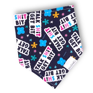 May include: Dark blue dog bandana featuring the text "TALK SHIT GET BIT" and "SHIT BIT" in white, pink, and blue. The bandana is patterned with floral and star motifs in various colours.