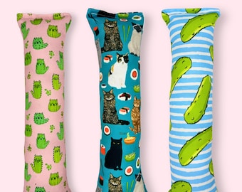 May include: Eco-Canvas Catnip & Silvervine Cat Toy. Three rectangular cat toys. One pink toy with green cat illustrations. A blue toy with cat and sushi illustrations. A blue and white striped toy with pickle illustrations.