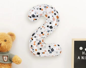 May include: A large, number 2 balloon with a white background and a pattern of black, orange, and gray squares. The balloon is inflated and appears to be made of foil. A teddy bear and a letter board are also in the image.