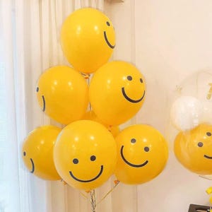 May include: A cluster of yellow smiley face balloons. Each balloon has a black curved line for a smile and a black dot for an eye. Some balloons are grouped together, while others are in a clear balloon.