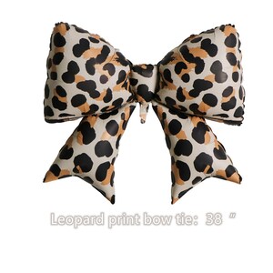 Könnte beinhalten: Eine große Fliege mit Leopardenmuster. Die Fliege hat einen cremefarbenen Hintergrund mit schwarzen und hellbraunen Flecken. Der Text "Leopard print bow tie: 38" befindet sich am unteren Rand des Bildes.