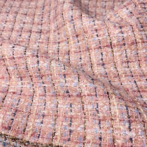 May include: Pink, blue, and gold tweed fabric with a subtle sheen. The fabric has a woven texture and a slightly frayed edge.