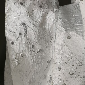 May include: White fabric with a silver metallic pattern. The pattern features abstract lines and dots.