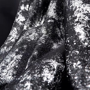 Puede incluir: Primer plano de una tela negra con un brillo metálico plateado. La tela tiene una textura casi arrugada.