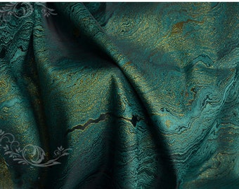 May include: Close-up of a teal fabric with a gold marbled pattern. The fabric has a subtle sheen and a textured surface.