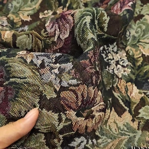 Könnte beinhalten: Ein gewebter Stoff mit einem dichten Blumenmuster in den Farben Dunkelgrün, tiefes Burgunderrot, Braun und Creme. Das Textil zeigt ein komplexes, mehrfarbiges Gobelingewebe mit sichtbaren Fäden und einer strukturierten Oberfläche.