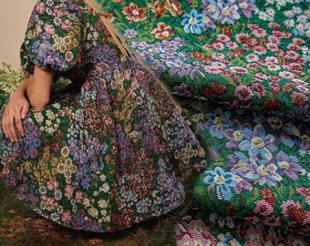 May include: A green dress with a floral pattern. The dress has a full skirt and short sleeves. The fabric is a tapestry-like weave.