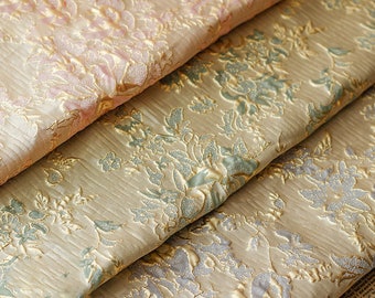 May include: Close-up of three fabric swatches with a floral damask pattern. The top swatch is pink, the middle swatch is green, and the bottom swatch is silver. All three swatches have a gold metallic thread woven into the fabric.