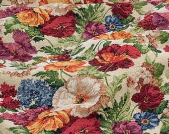 May include: Close-up of a floral tapestry featuring a repeating pattern of colorful flowers. The flowers include red, orange, purple, and blue blooms with green leaves against a beige background. The fabric has a woven texture.