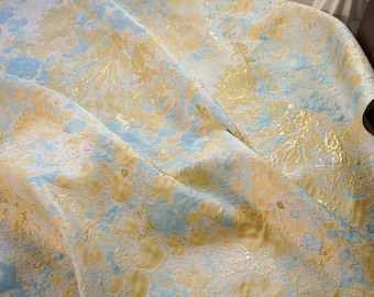 May include: A blue and gold fabric with a floral pattern. The fabric is textured and has a metallic sheen.