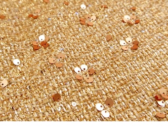 May include: Close-up of a textured fabric with a woven appearance. The fabric is a warm gold color, with scattered copper-colored sequins and small white sequins. The sequins add a touch of sparkle to the material.