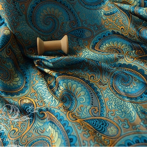 Könnte beinhalten: Tealfarbener und goldfarbener Stoff mit Paisley-Muster und einer Holzspule mit Garn darauf.
