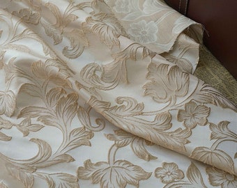 May include: Close-up of a cream-colored fabric with a raised floral pattern in a gold color. The fabric is soft and luxurious, perfect for upholstery or curtains.