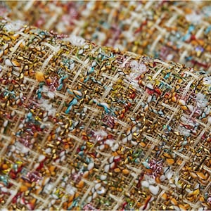 Puede incluir: Primer plano de una tela de tweed beige con textura tejida. La tela está entrelazada con hilos de colores, incluyendo rojo, azul, verde y dorado.