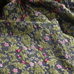 Op de afbeelding: Close-up van een blauwe stof met een groen en roze bloemenpatroon. De stof heeft een textuur, een verhoogd ontwerp.