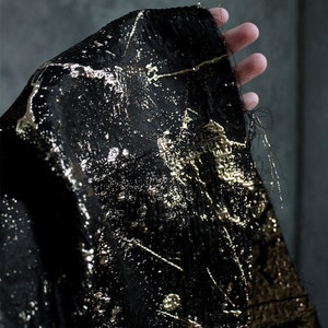 May include: Black fabric with gold metallic accents. The fabric has a textured, crinkled look and is decorated with a scattered pattern of gold paint.