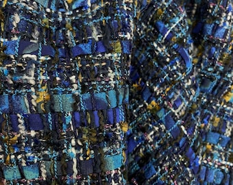May include: Close-up of a blue, green, and gold tweed fabric with a woven texture. The fabric has a subtle shimmer and is perfect for a jacket or skirt.