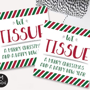 May include: Two white rectangular gift tags with red and green striped borders. The tags read "WE TISSUE" in red script, with the text "A MERRY CHRISTMAS AND A HAPPY NEW YEAR" in green below. A black and white string is in the background.