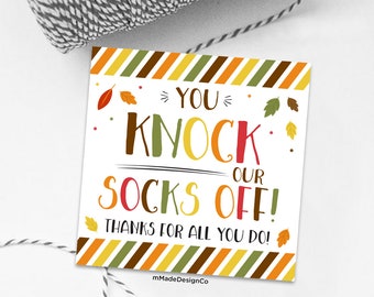 May include: A square white gift tag with the text "YOU KNOCK OUR SOCKS OFF! THANKS FOR ALL YOU DO!" in various colors. The tag has a fall-themed border with orange, yellow, green, and brown stripes and leaf accents.