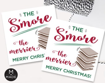 Op de afbeelding: Twee witte vierkante kaarten met de tekst "THE S'more the merrier MERRY CHRISTMAS!" in rood en groen. Elke kaart heeft een afbeelding van een stapel s'mores.