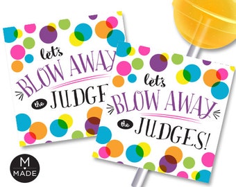 May include: Two colourful lollipop sticks with a white background and polka dots. The text on the sticks reads "Let's Blow Away the Judge" and "Let's Blow Away the Judges".