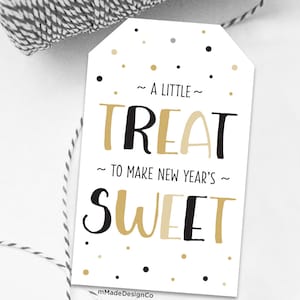 Peut inclure: Une étiquette cadeau blanche avec des confettis noirs et dorés. L'étiquette dit "Un petit plaisir pour rendre le Nouvel An doux".