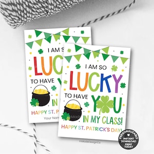 May include: Two St. Patrick's Day cards with the text "I am so lucky to have you in my class!" in colorful letters. Each card features a pot of gold, shamrocks, and a banner. The cards are on a white surface.