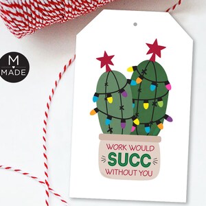 May include: A white gift tag with a cartoon illustration of two green cacti decorated with colorful lights and red star toppers. The tag reads "WORK WOULD SUCC WITHOUT YOU" in a playful font. Red and white twine is visible.