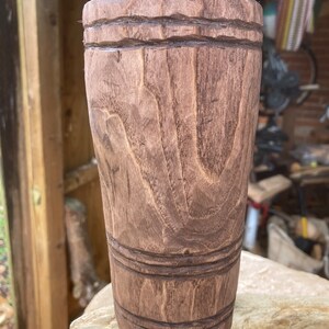 Puede incluir: Una taza de madera marr&oacute;n con un dise&ntilde;o tallado. La taza tiene un fondo liso y redondeado y una parte superior ancha y abierta.