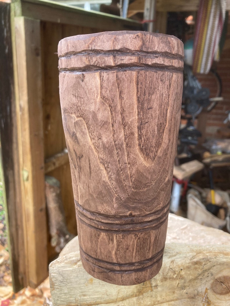 Puede incluir: Una taza de madera marr&oacute;n con un dise&ntilde;o tallado. La taza tiene un fondo liso y redondeado y una parte superior ancha y abierta.